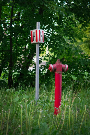 Red fire hydrant standing on grassy ground next to a small metal sign marked with the letter H, indicating a hydrant location.の写真素材