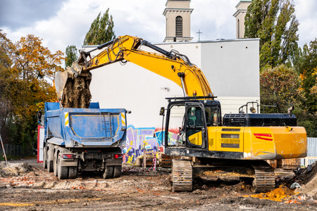 Excavator loading soil into a dump truck at a construction site under daylight conditions.の写真素材