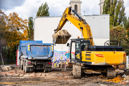Excavator loading soil into a dump truck at a construction site under daylight conditions.の写真素材