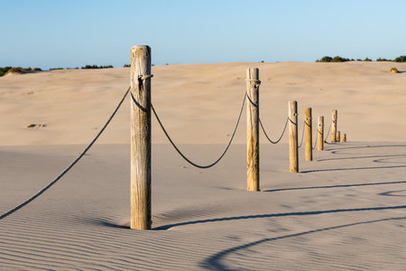Wooden posts connected by a rope, standing in sandy terrain. A simple natural scene often used to mark paths or boundaries in coastal or desert landscapes.の写真素材