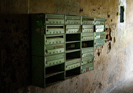 Close-up of rusty vintage mailboxes inside an abandoned house. The peeling paint and decay create a nostalgic and mysterious atmosphere.の写真素材