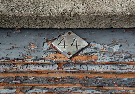 A metal diamond-shaped plate with the number 44 attached to an old wooden door with peeling paint, showing signs of age and wear.の写真素材