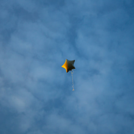 A bright helium balloon shaped like a star gently rises against a clear sky, bringing a sense of lightness and celebration.の写真素材