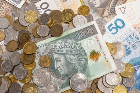A mixed spread of Polish money featuring scattered coins and zloty banknotes, with one bill partially hidden under a coin, creating a detailed financial texture.の写真素材