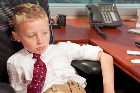 Cute Young Boy in Business Office with Bored Expressionの写真素材