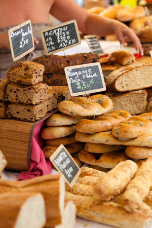 Freshly baked gourmet bread on sale from a outdoor market in Paris, France with a woman in the background のeditorial素材