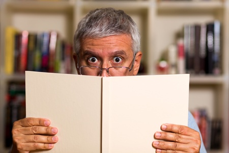 Handsome middle age man reading a book with a bookcase background 