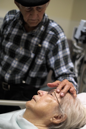 Elderly 80 plus year old woman in a hospital bed with her caring husband 
