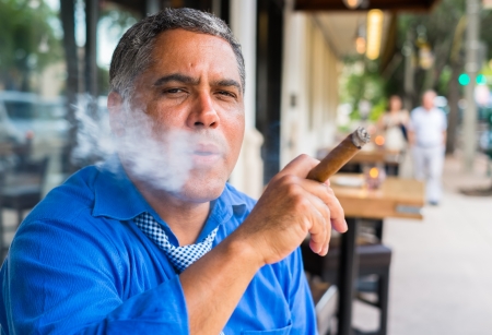 Handsome middle age Hispanic man smoking a cigar outdoors in a restaurant.の写真素材