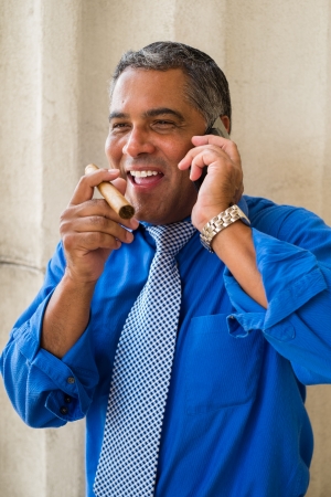 Handsome middle age Hispanic man smoking a cigar outdoors and speaking in a wireless phone in a urban setting.の写真素材