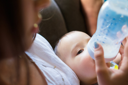 Cute baby boy being fed milk by his mother in a home setting.の写真素材