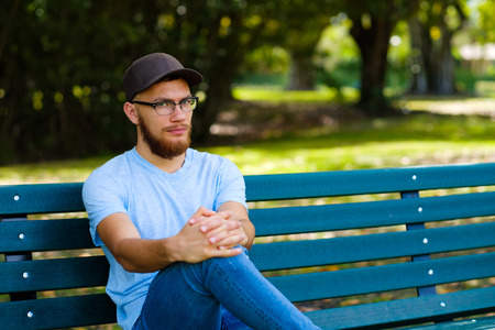 Handsome young man with a beard sitting on a park bench.の写真素材