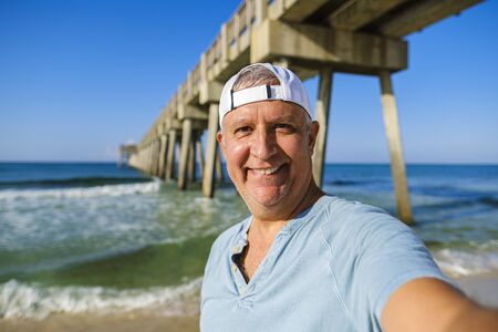 Handsome man enjoying the beach with a pier in the background.