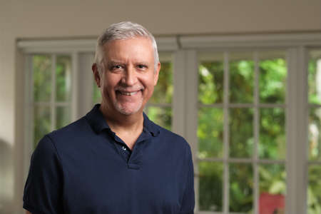 Handsome senior man portrait in a home setting holding a cell phone.