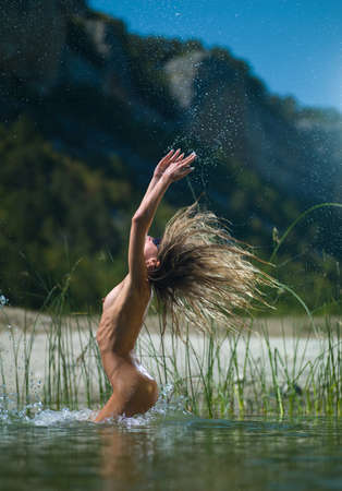 Nude girl jumping in the water against the backdrop of the mountainsの写真素材