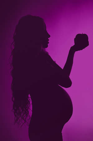 Photo of pregnant woman in black, holding an apple in his hand