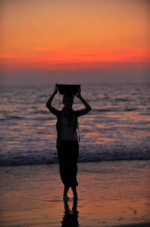 a girl holding a basket on her head at sunset in Indiaの写真素材
