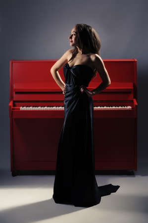 Photo of a beautiful girl standing on a piano in an elegant evening dressの写真素材