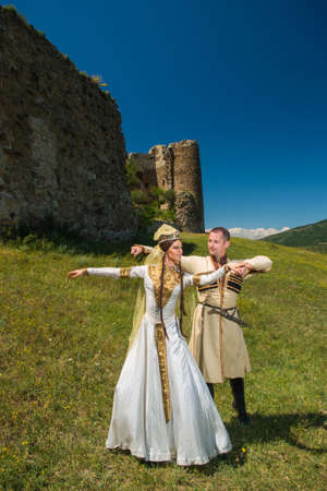 A man and a woman in Georgian national clothes outdoors on a background of an old building