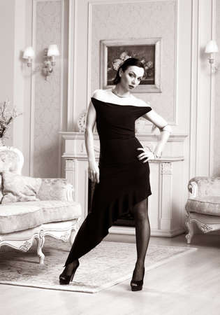 Beautiful woman in a black dress standing in the interiorの写真素材