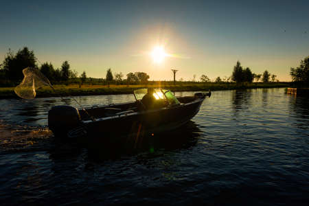A fisherman on a boat at dawn goes fishing.