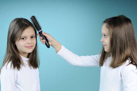 white twin girl arranging her sister hair with brushの写真素材