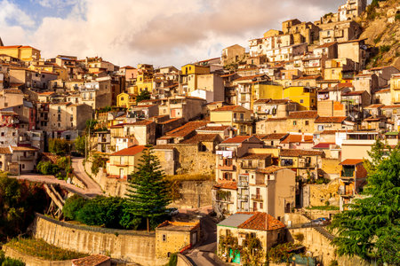 old mediterranean mountain dense town with levels of yellow houses and terraces on a steep mountain in evening light, vintage european village on a rockの写真素材