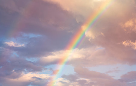 amazing bright rainbow in beautiful evening blue cloudy sky after rain and thunder with flash sun light streaming thruogh the clouds, weather thunderstorm conceptの写真素材