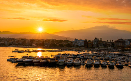 picturesque sunrise or sunset in a sea port with a gulf dock pier with tour boats and a town with cloudy sky on background of a seashore landscapeの写真素材