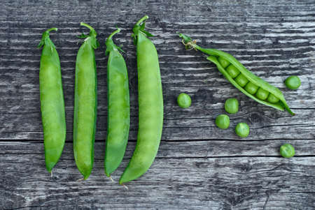 Green pea pods beautifully lie on vintage wooden surfaces, top view