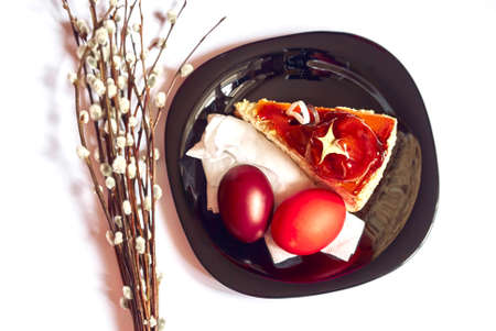 Stylish black plate with piece of cake, twigs of willow and Easter eggs, isolated white background