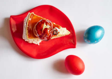 Stylish red plate with piece of cake and Easter eggs on white backgroundの写真素材