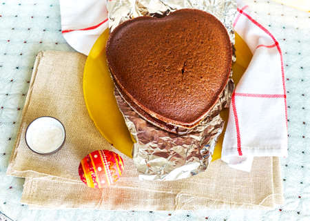 Freshly baked sponge cake in the shape of heart and souvenir Easter egg on the tableの写真素材