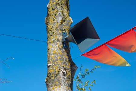 The loudspeaker on tree on background of blue sky and red holiday flags, victory day, holiday victoryの写真素材