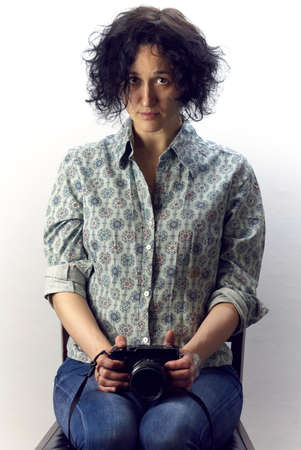 Young woman with black curly hair holding camera in his hands sitting on chair and looks at the...