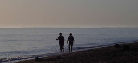 Two women walk along sea coast and communicate. Sea panoramic view