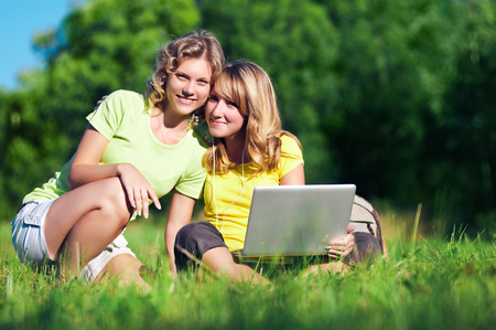 Two happy girl with laptop in summer parkの写真素材