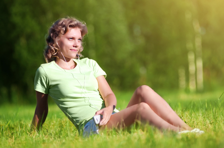 Smiling girl is sitting on grass and listening the musicの写真素材