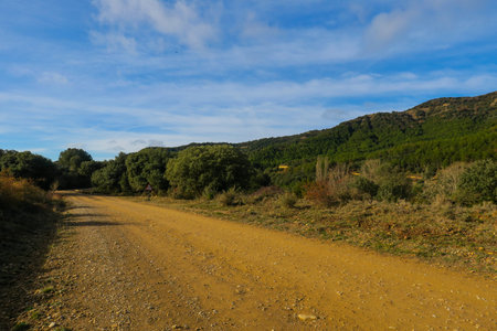 Gravel road in the mountains under blue sky with white clouds.の写真素材