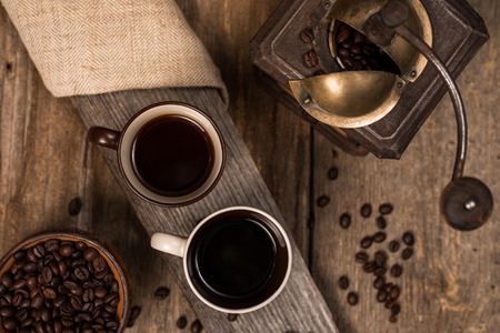 Coffee beans and two cups of coffee on the old rustic wooden table with empty space for graphic designの写真素材