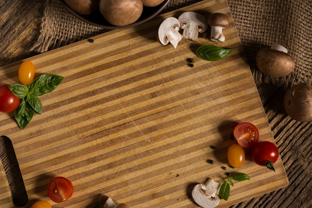 old rustic bamboo plate on the old wooden table with vegetables, tomato, basil, papper, mushroom and empty space for text or graphic designの写真素材