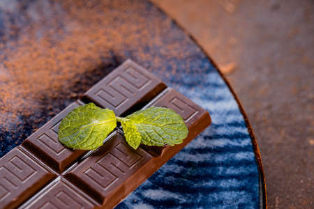 Chocolate bar with green mint leaf on blue textured ceramic plate