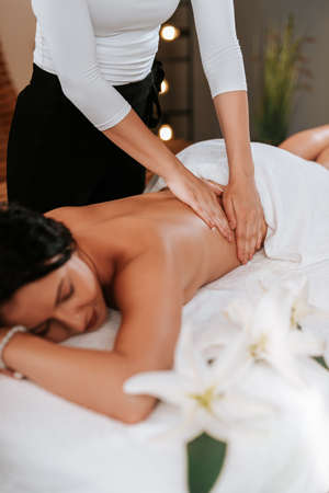Beautiful young woman in the massage salon with brown curly hair and healthy skin. Masseur and...