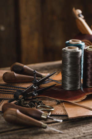 Leather craft tools on the old wood table in a shed. Leather craftsman workspace. Grounge dark wood...