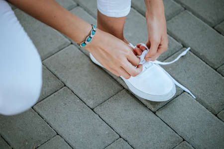 young girl tie her white shoelaces at the street