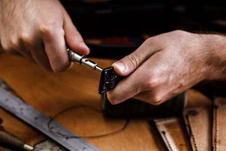Close up of a shoemaker or artisan worker hands. Leather craft tools on old wood table. Leather...