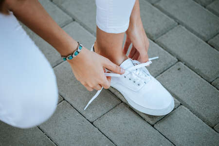 young girl tie her white shoelaces at the streetの写真素材