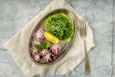 Delicious mini boiled octopus and fresh wakame seaweed salad with sesame seeds and lemon....