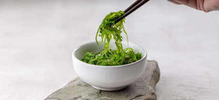 Croped photo of green wakame seaweed salad with chopstick at the restaurant