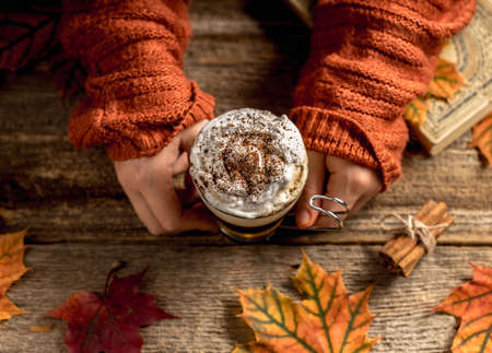 Hand holding warm pumpkin spice latte or coffee. Autumn style flat lay. Cozy warm image of a girl hands with a cup of delicious drink.の写真素材